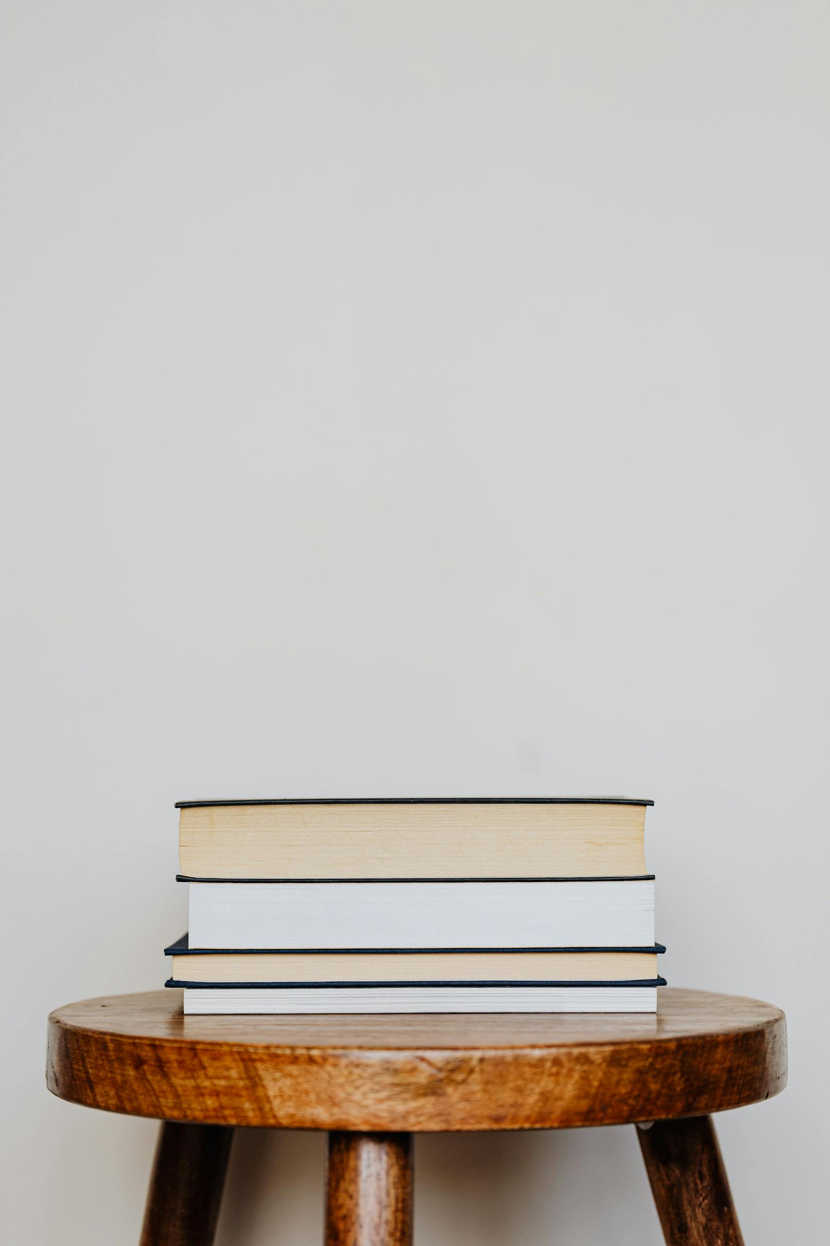 Close-up of three hardcover books stacked on a wooden stool against a plain background.
